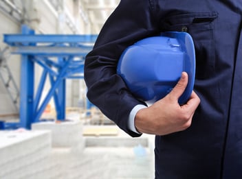 Factory worker with blue hard hat and plan scene behind him