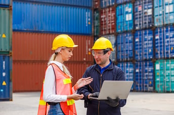 Two workers with computer in front of shipping containers in a port