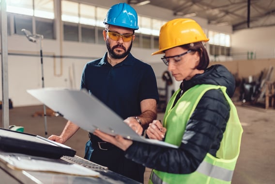 male-female-workers-hardhats-reviewing-plans-on-plant-floor