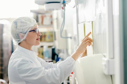 woman-in-white-labcoat-and-hairnet-reading-instructions-on-wall